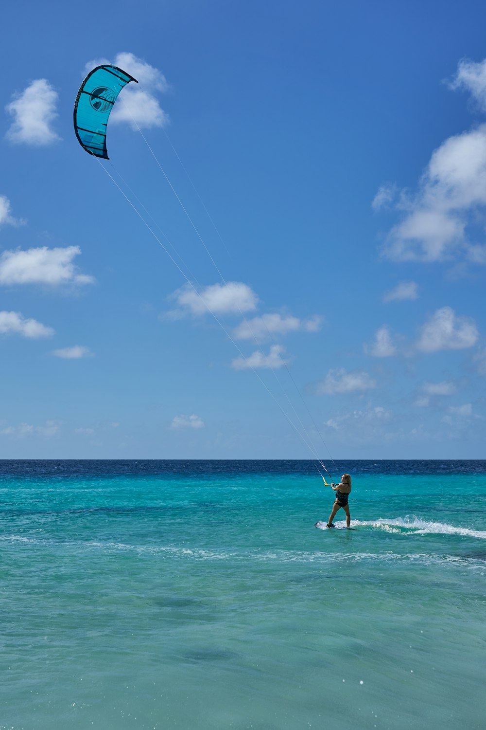 woman in white and black bikini holding blue and white kite surfing on sea during daytime