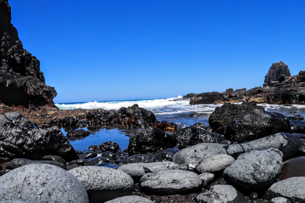 rocky shore with ocean waves crashing on rocks under blue sky during daytime