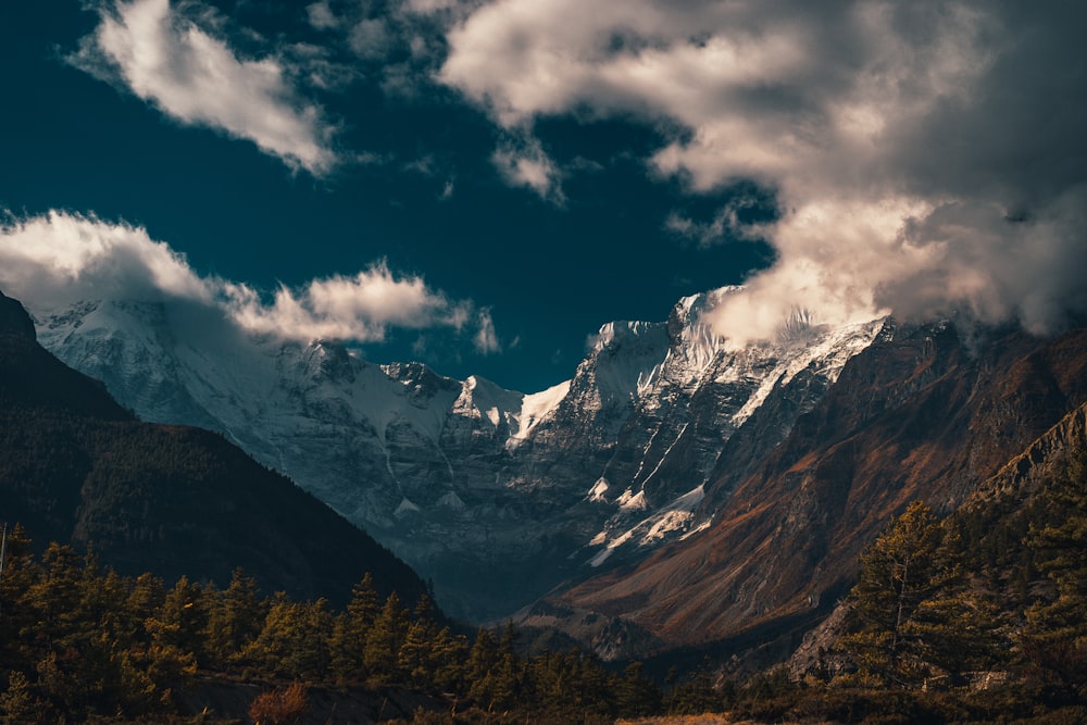 green trees near snow covered mountain under blue and white cloudy sky during daytime