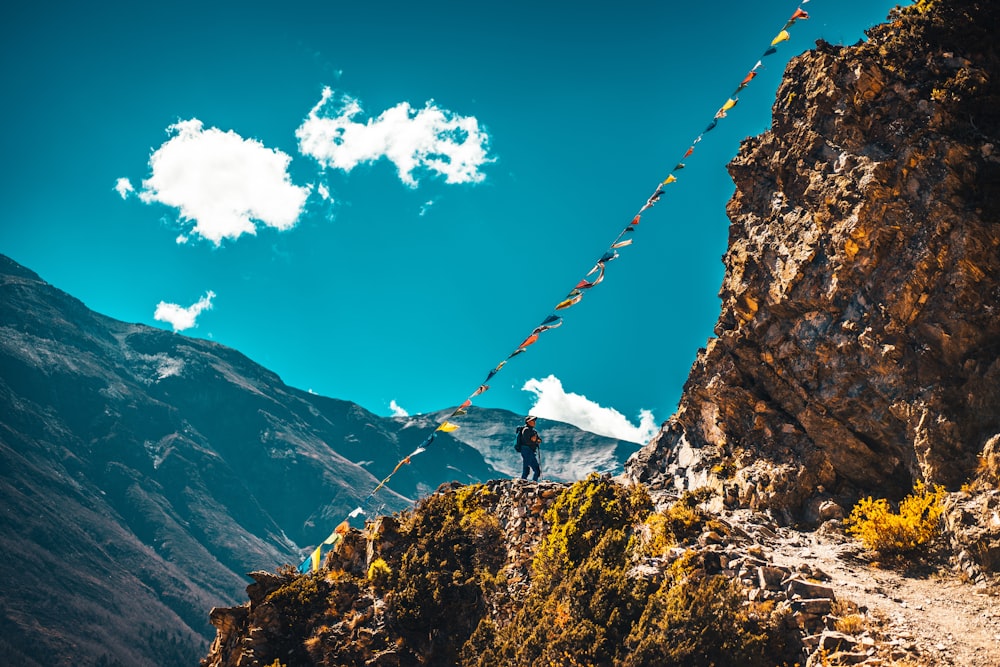 person in white shirt and black pants standing on rock mountain under blue sky during daytime