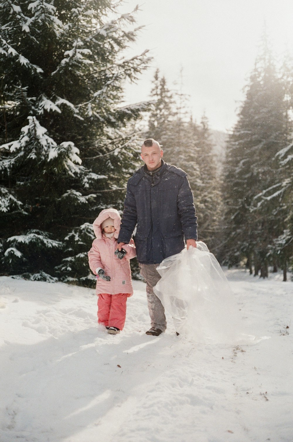 man in black jacket holding girl in pink coat on snow covered ground during daytime