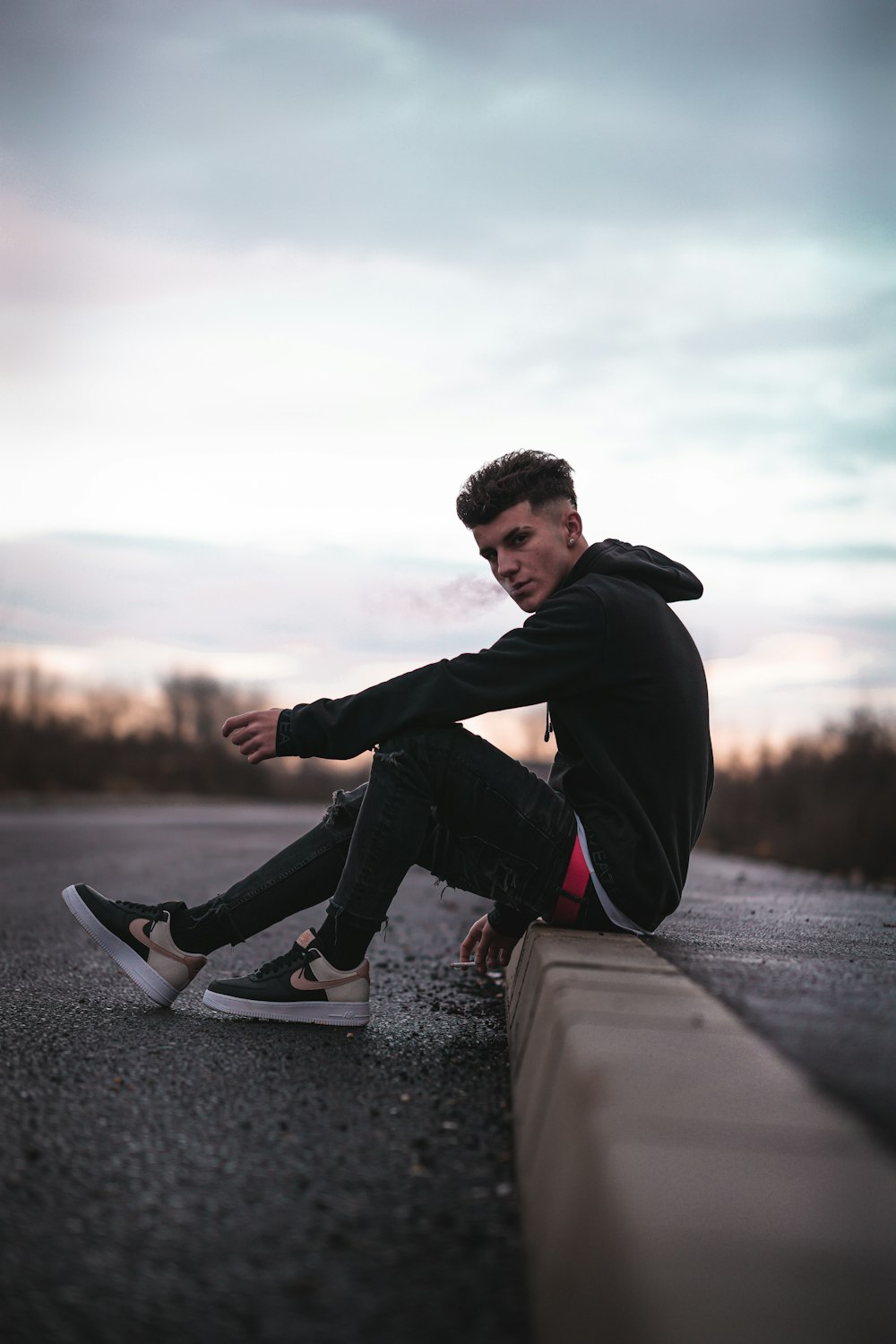 man in black hoodie and black pants sitting on concrete bench