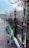 Several green electric scooters are lined up against a black wrought iron fence on a snow-dusted sidewalk. Leafless trees and classic street lamps can be seen, with people walking in the distance. A modern building is visible on the street corner, creating an urban, wintry setting.