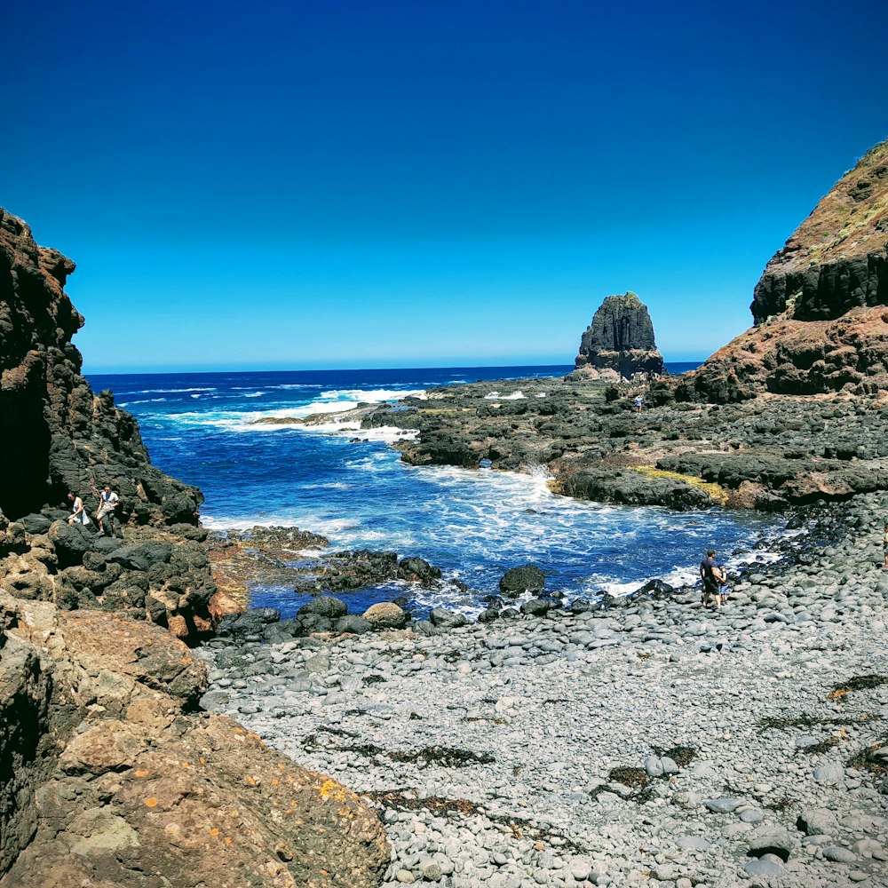 brown rocky mountain beside sea under blue sky during daytime