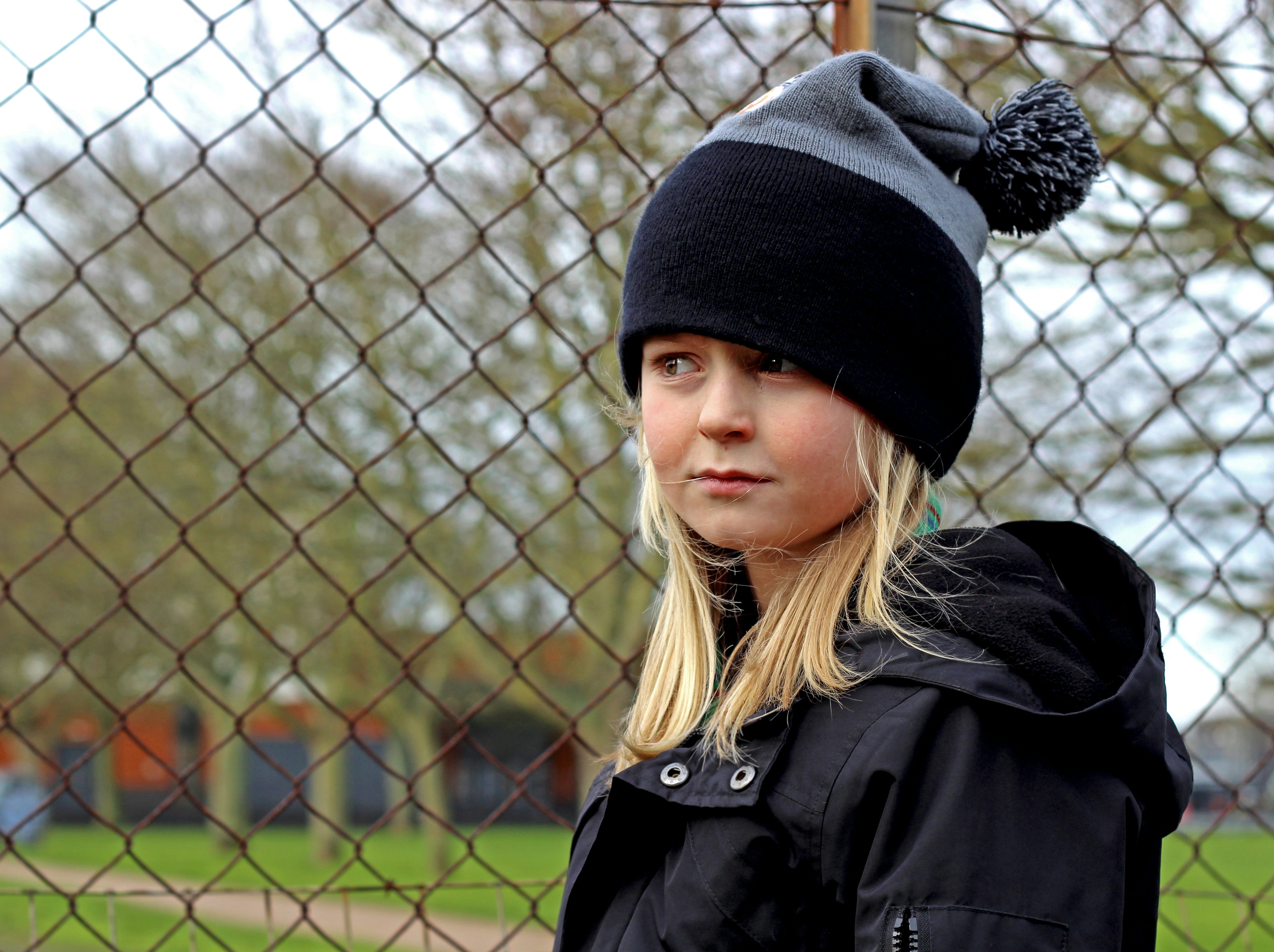 woman in black knit cap and black coat standing near gray metal fence during daytime
