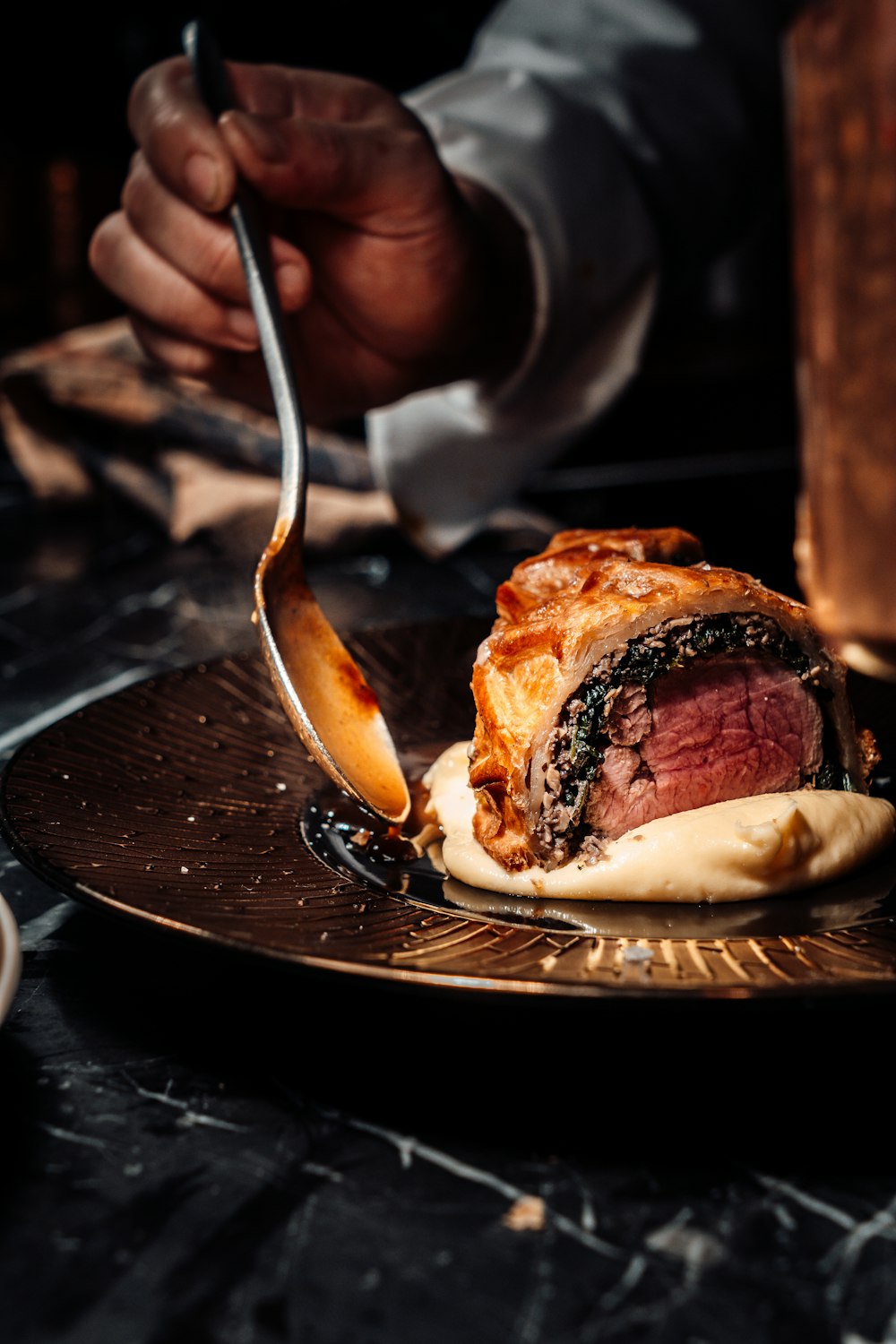 person holding stainless steel fork and knife slicing meat on black ceramic plate