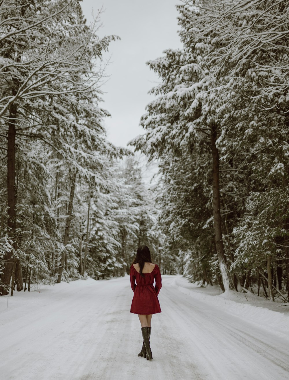 woman in red coat standing on snow covered ground surrounded by trees during daytime