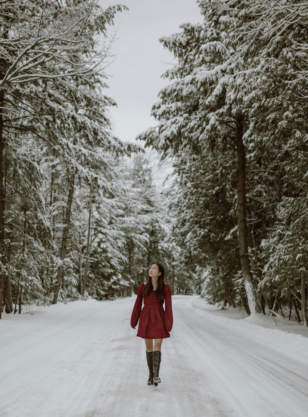 woman in red coat standing on snow covered ground surrounded by trees during daytime