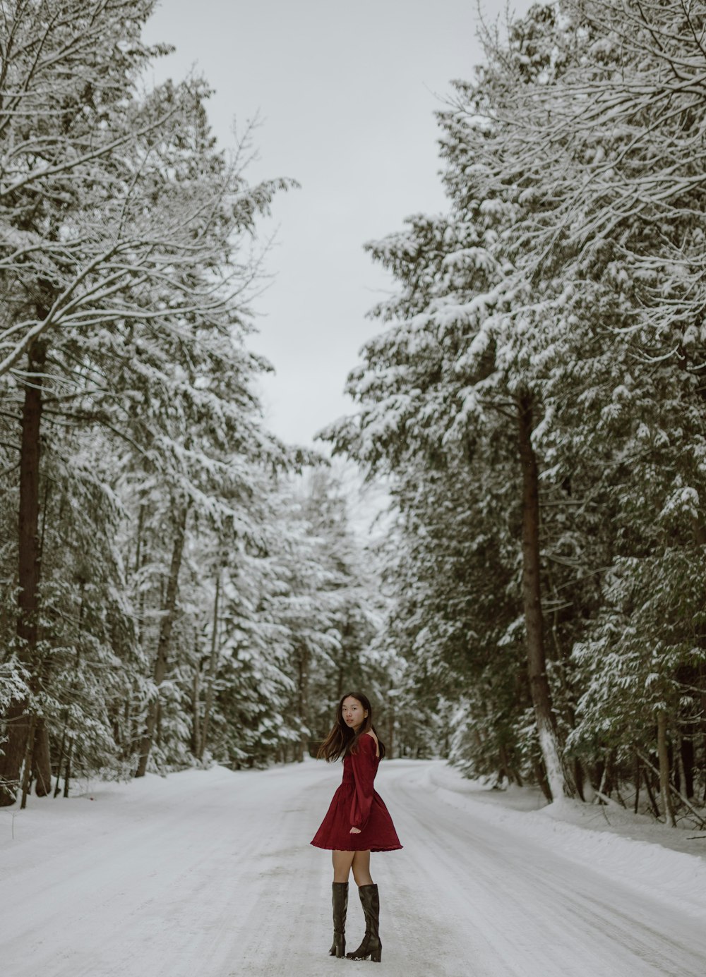 woman in red coat standing on snow covered ground near trees during daytime