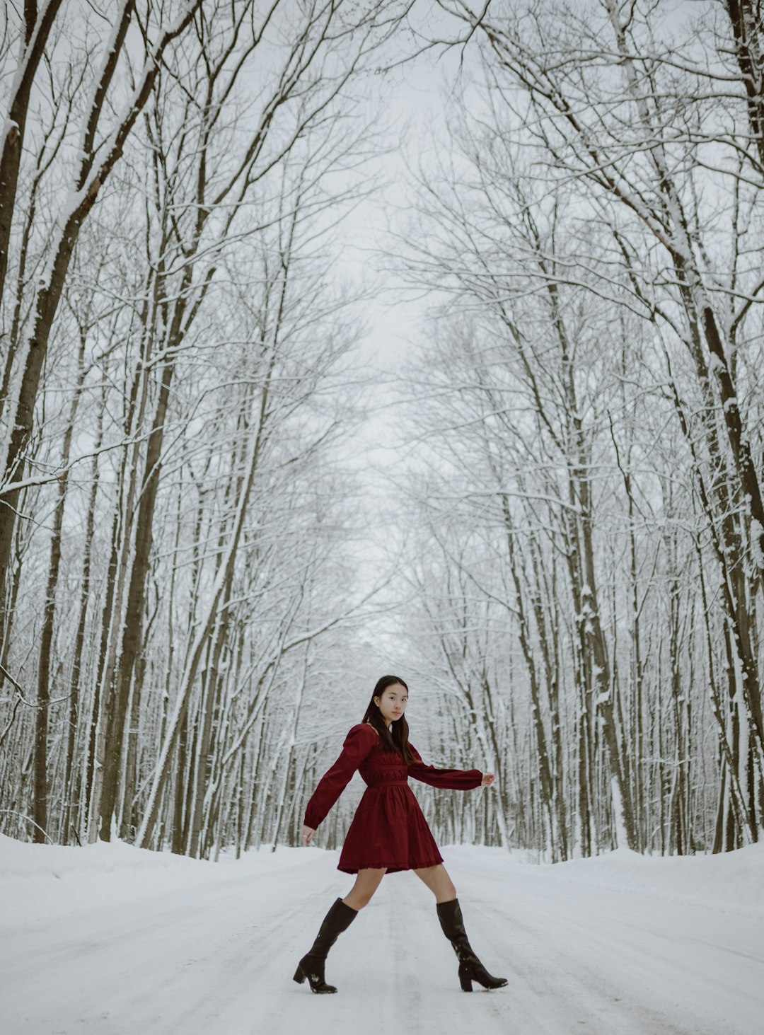 woman in red coat standing on snow covered ground surrounded by bare trees during daytime