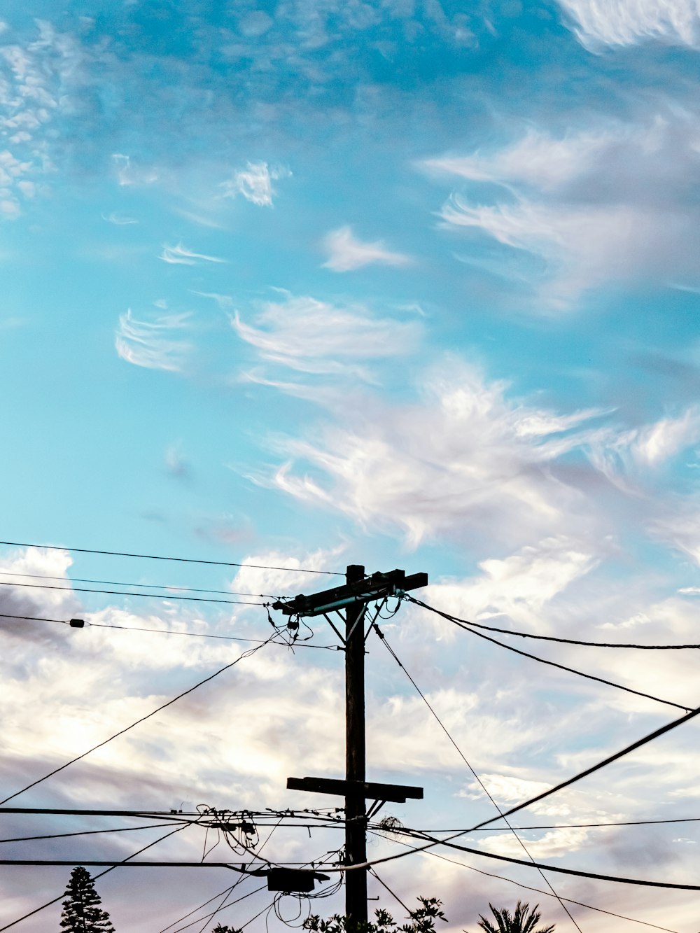 poteau électrique noir sous ciel bleu et nuages blancs pendant la journée