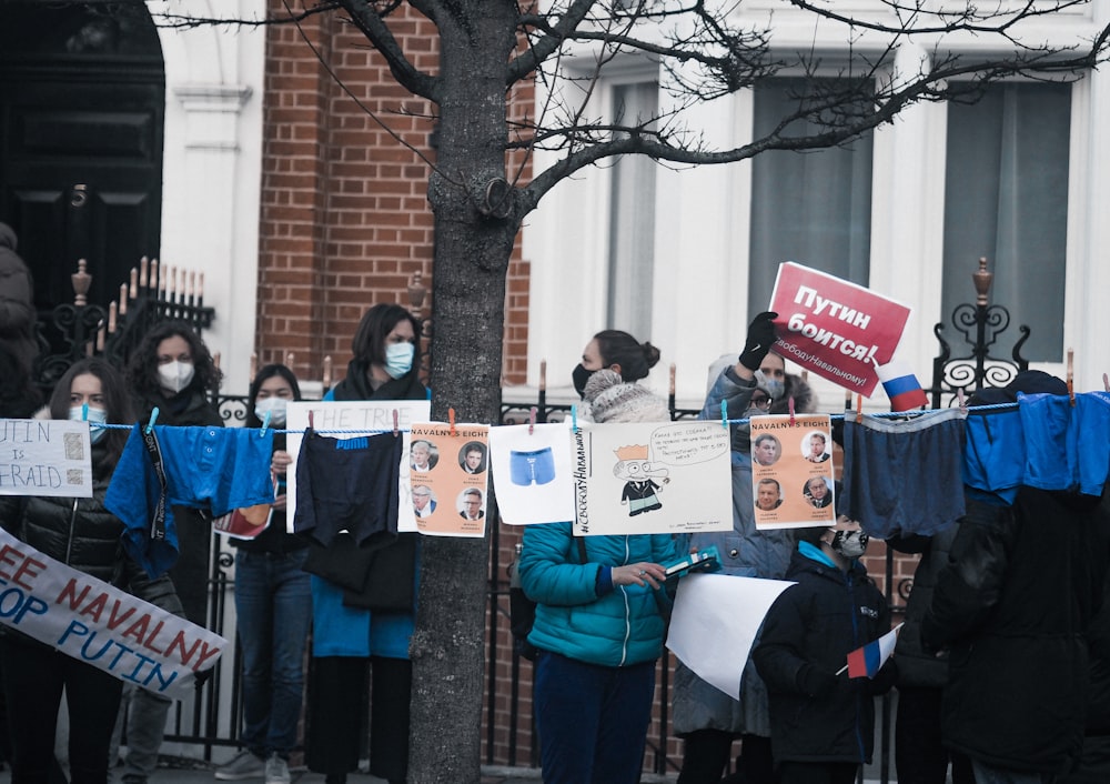 people holding white and blue banner near bare tree during daytime