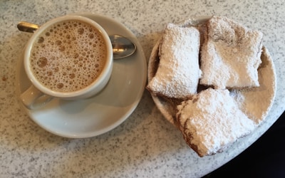 Rustic wooden tray filled with steaming hot, powdered sugar-dusted beignets beside a vintage coffee cup of rich chicory coffee.