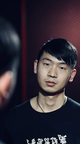 Model wearing a dark grey t-shirt with a bold, abstract rock band emblem under moody lighting.