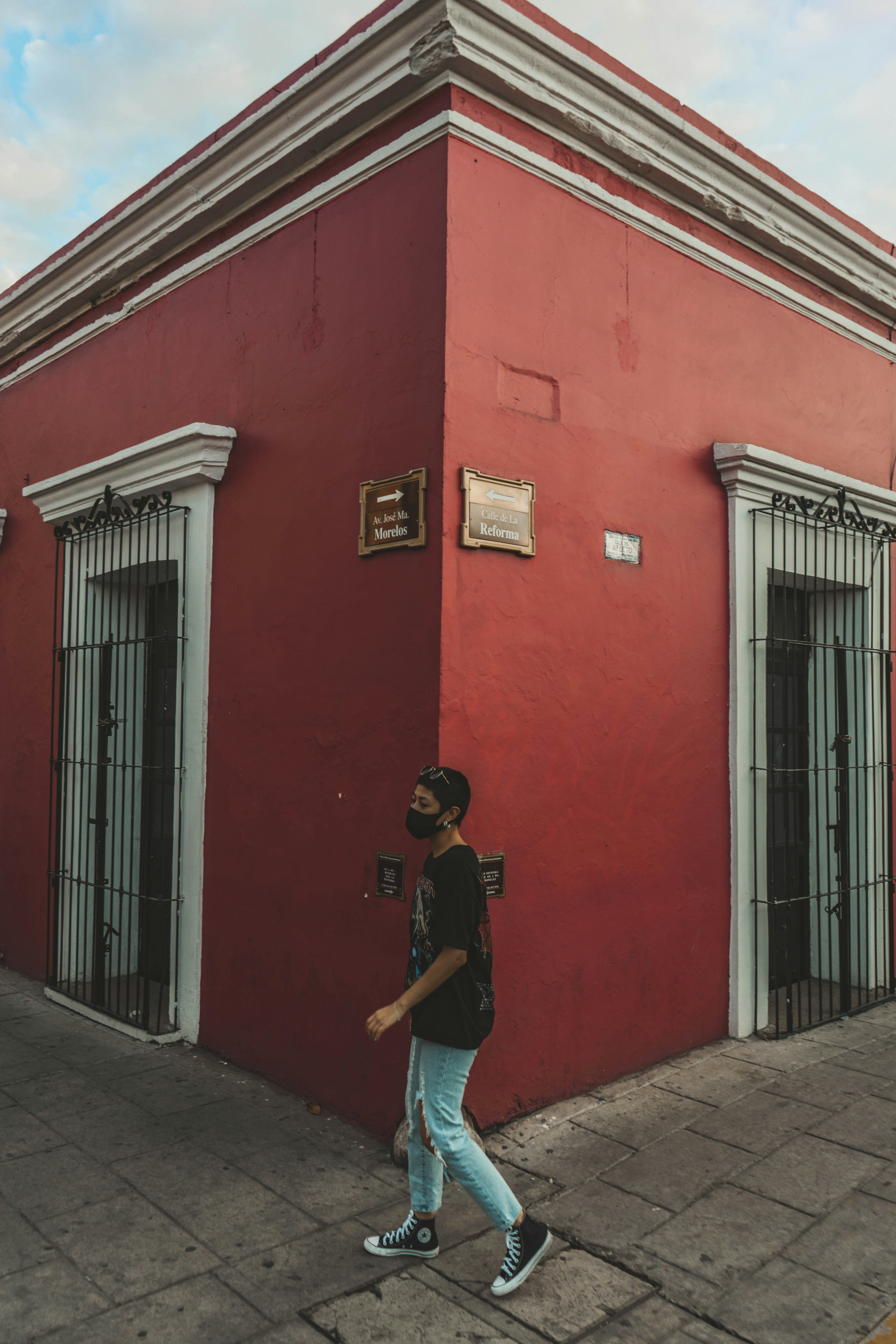 woman in black t-shirt and blue denim jeans standing beside red concrete building during daytime
