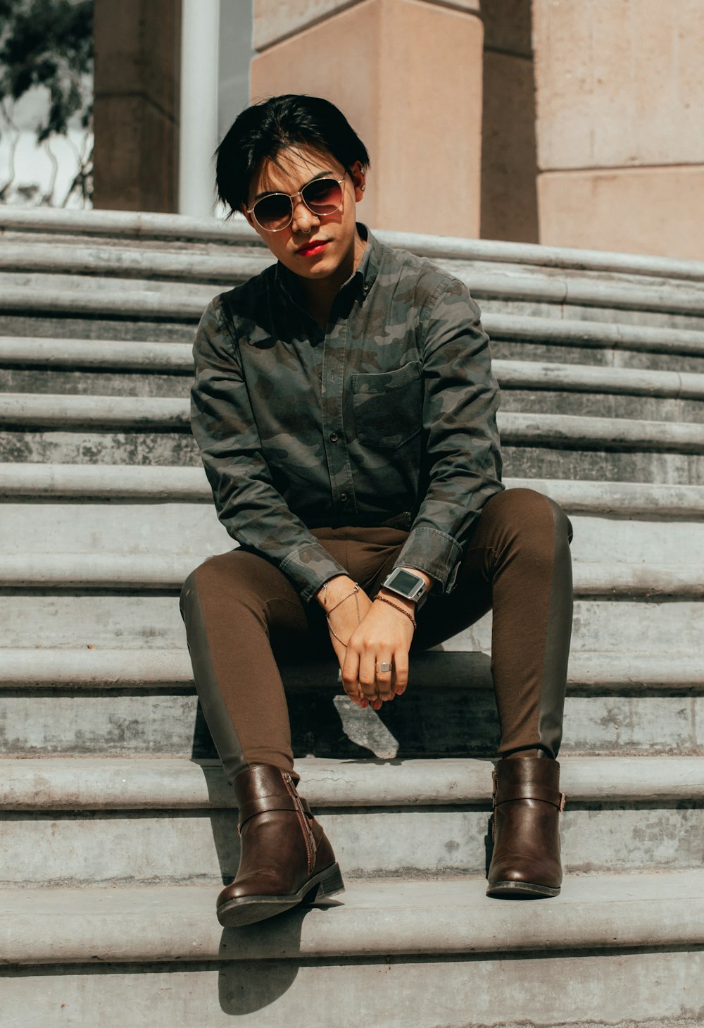 woman in black leather jacket and brown pants sitting on white concrete stairs