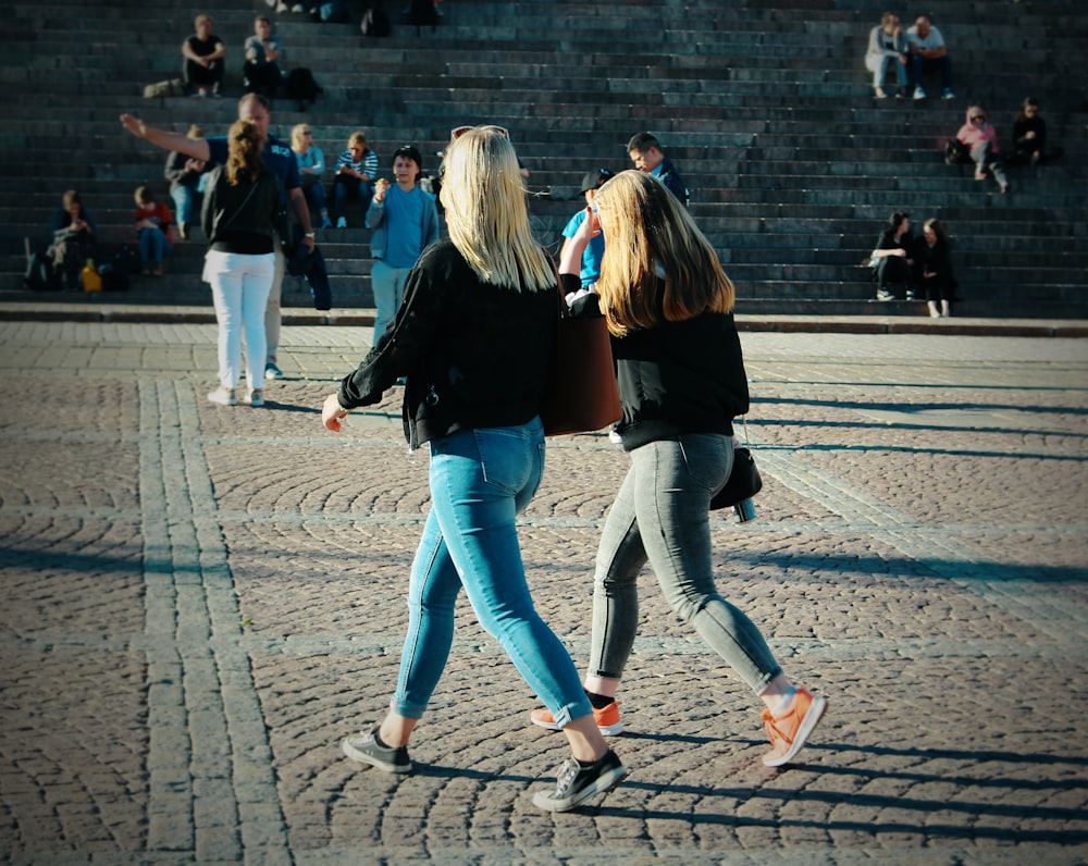 woman in black jacket and blue denim jeans walking on street during daytime