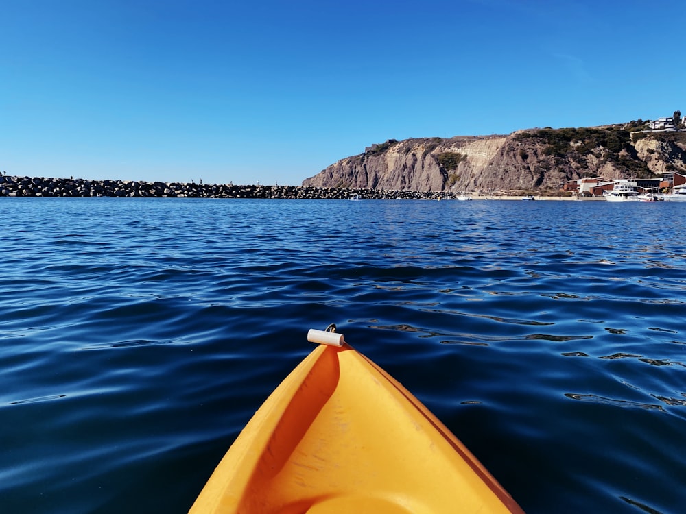 yellow kayak on blue sea near brown and green mountain under blue sky during daytime