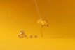 A collection of gold jewelry is set against a vibrant yellow background. The pieces include a ring, earrings, and a necklace, all designed to resemble a ginkgo leaf. The shiny metallic finish of the jewelry contrasts with the matte yellow surface.