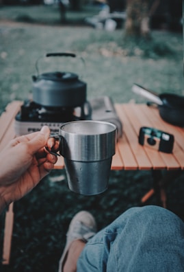 A user comfortably holding a portable urinal while camping outdoors.