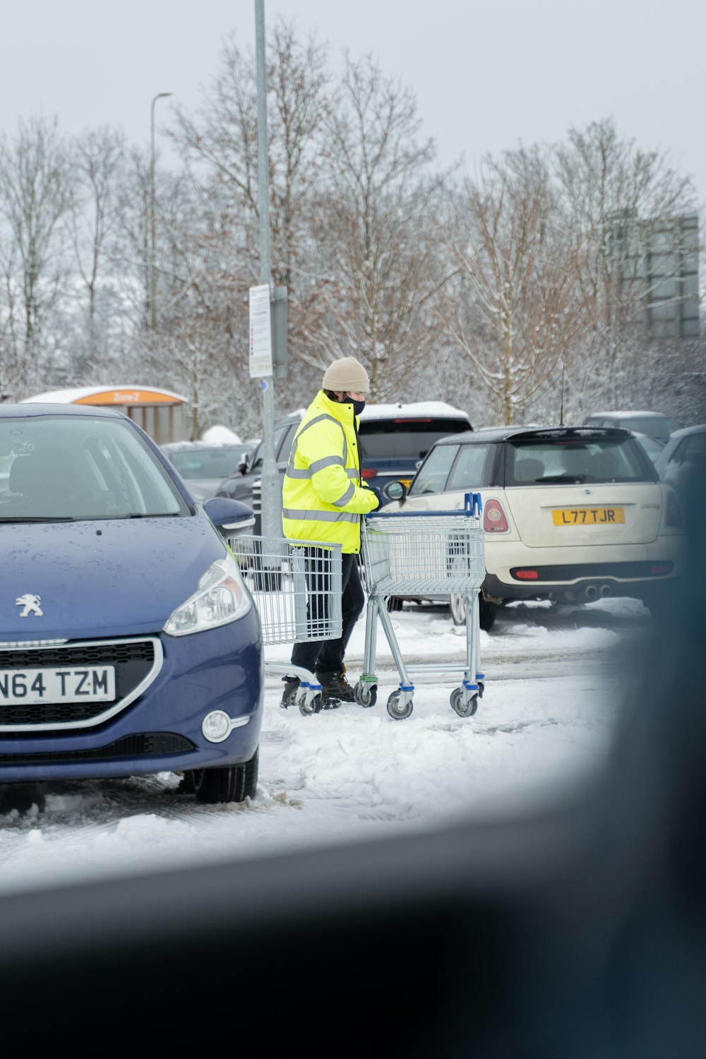 man in yellow jacket and white knit cap standing beside blue honda car during daytime