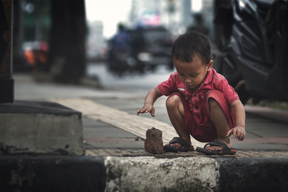 boy in red crew neck t-shirt sitting on concrete pavement during daytime