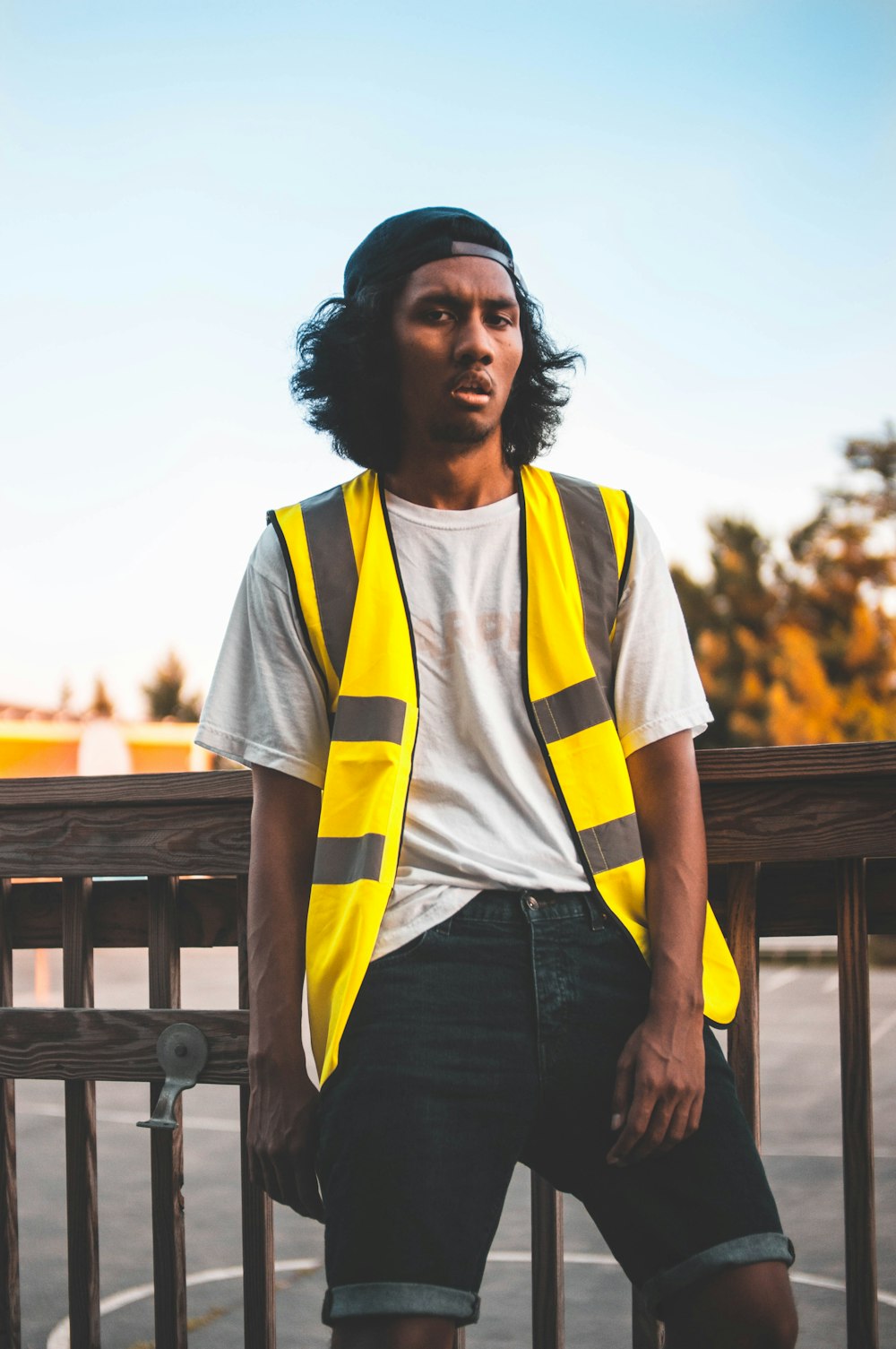 woman in yellow and white shirt and blue denim jeans standing near brown wooden bench during