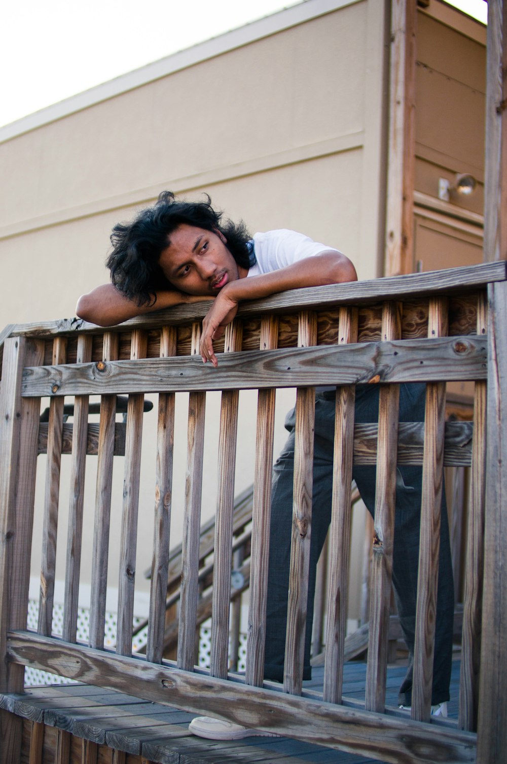 woman in white t-shirt leaning on brown wooden fence during daytime