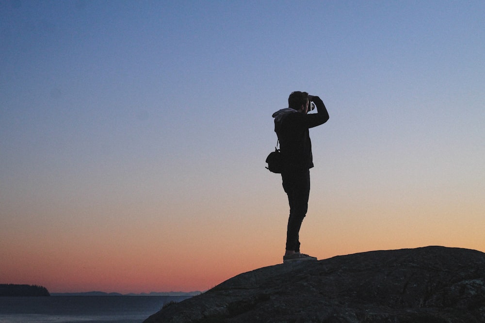 silhouette of man standing on rock formation during sunset