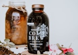 A bottle of Starbucks Cold Brew coffee is prominently displayed alongside a jar filled with coffee beans. Decorative flowers and leaves adorn the scene, adding elegance. Coffee beans are scattered around for an aesthetic touch.