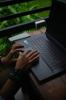 Close-up of hands managing social media posts on a laptop with green plants nearby