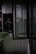 A slightly open glass door in a dark and industrial setting with corrugated metal walls. Large leaves are visible in the foreground, suggesting a juxtaposition of nature against the manufactured structure.
