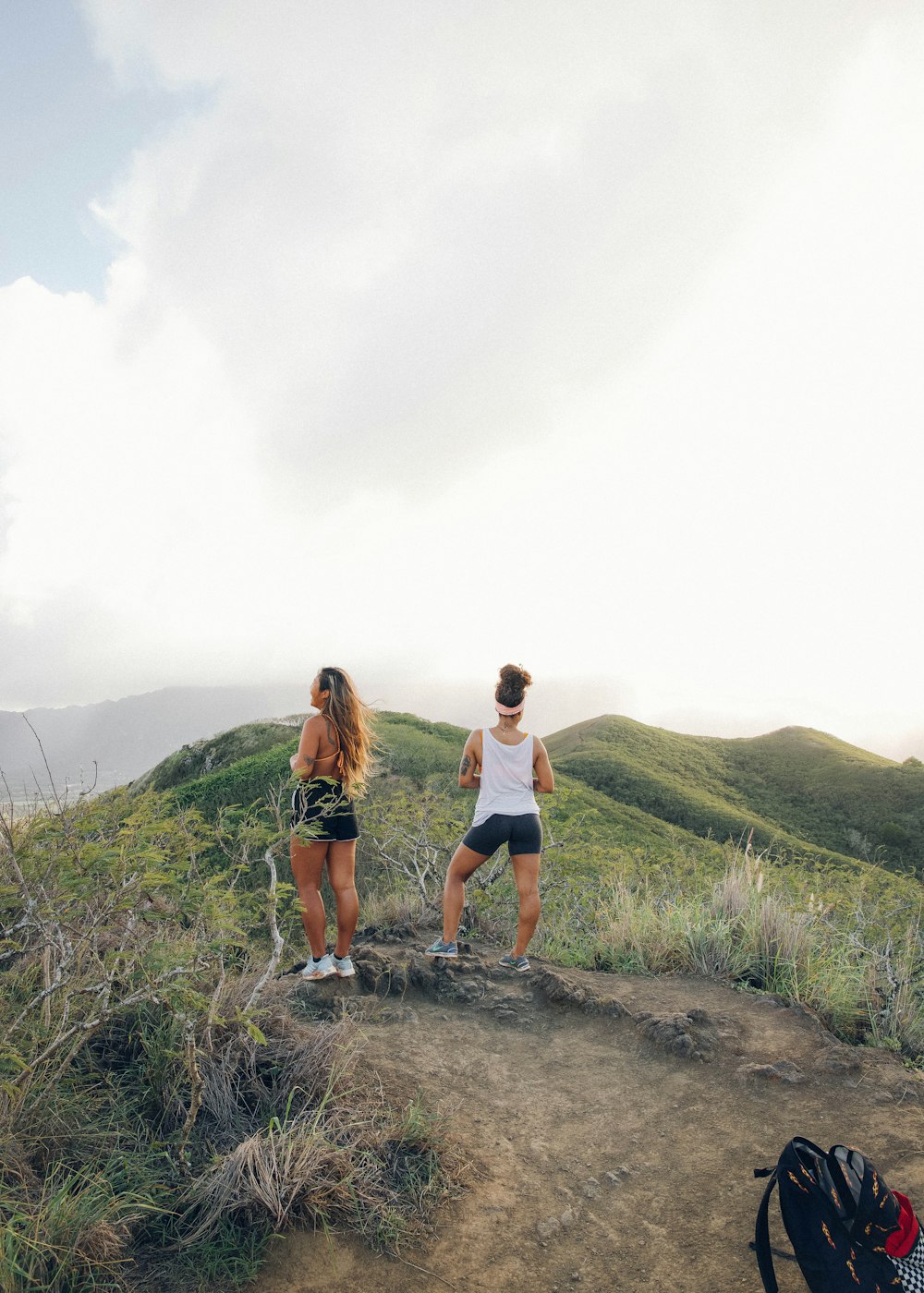 2 women standing on brown dirt road near green grass field during daytime