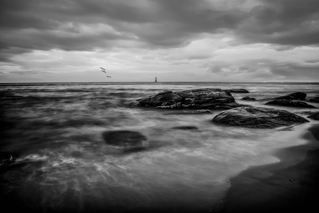 grayscale photo of person standing on rock formation near body of water