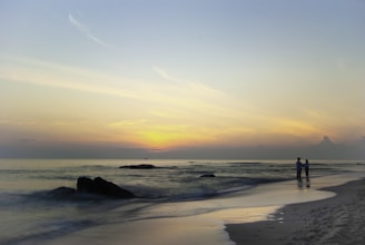 A soft rose-colored setting with a gentle hand holding another on a beach at sunset.