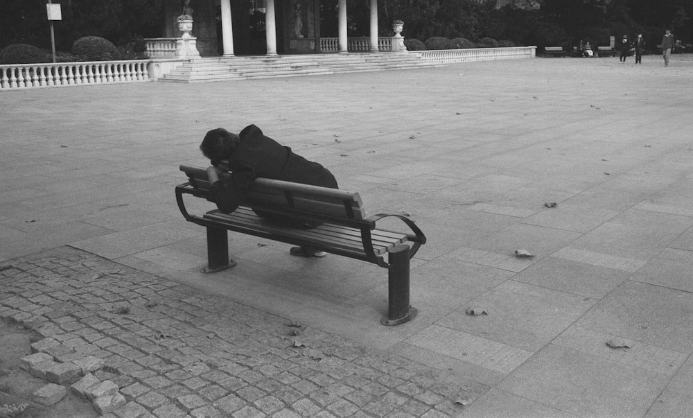 man sitting on bench in grayscale photography