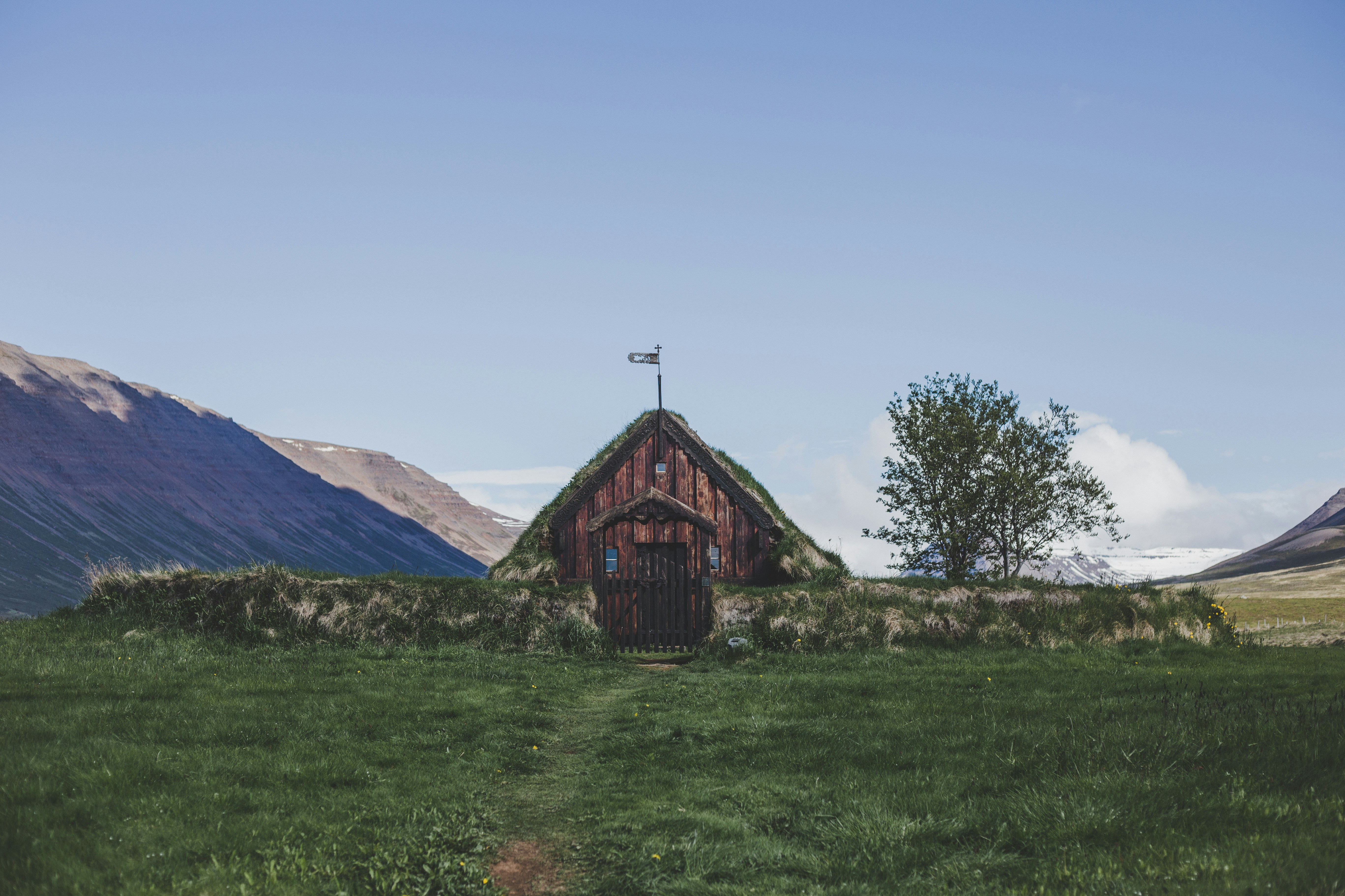 brown wooden house on green grass field near green trees and mountain during daytime