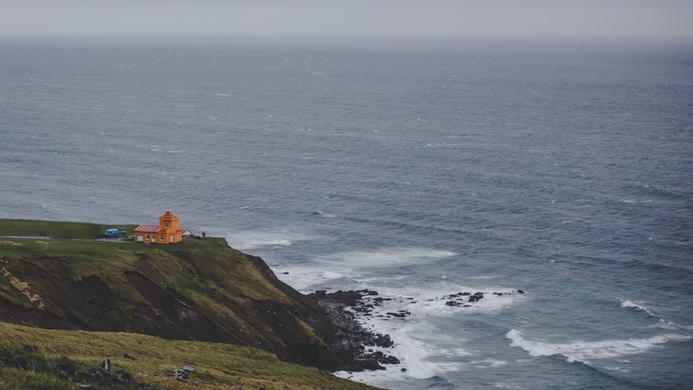 white and brown lighthouse on green mountain beside sea during daytime