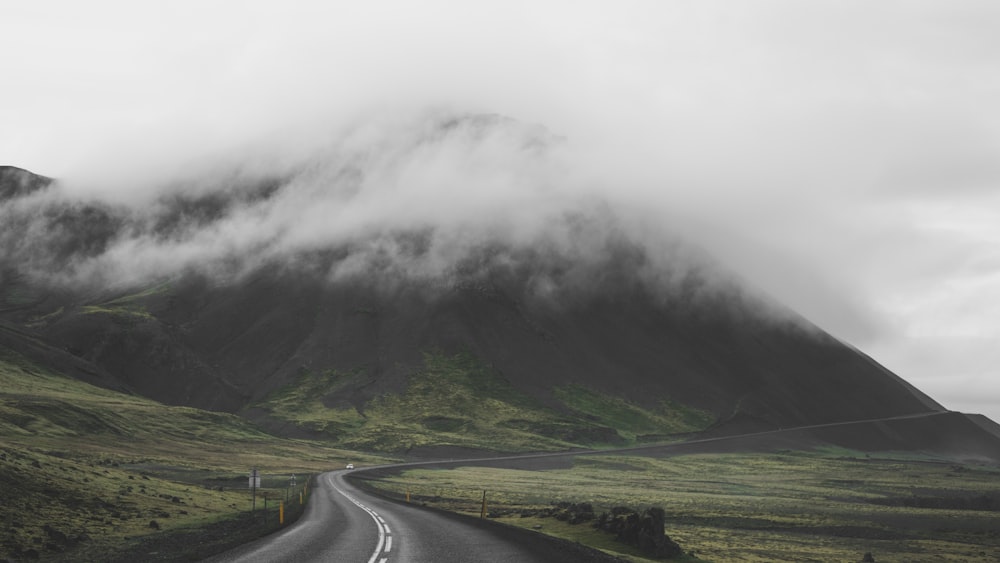 gray asphalt road near green grass field and mountain