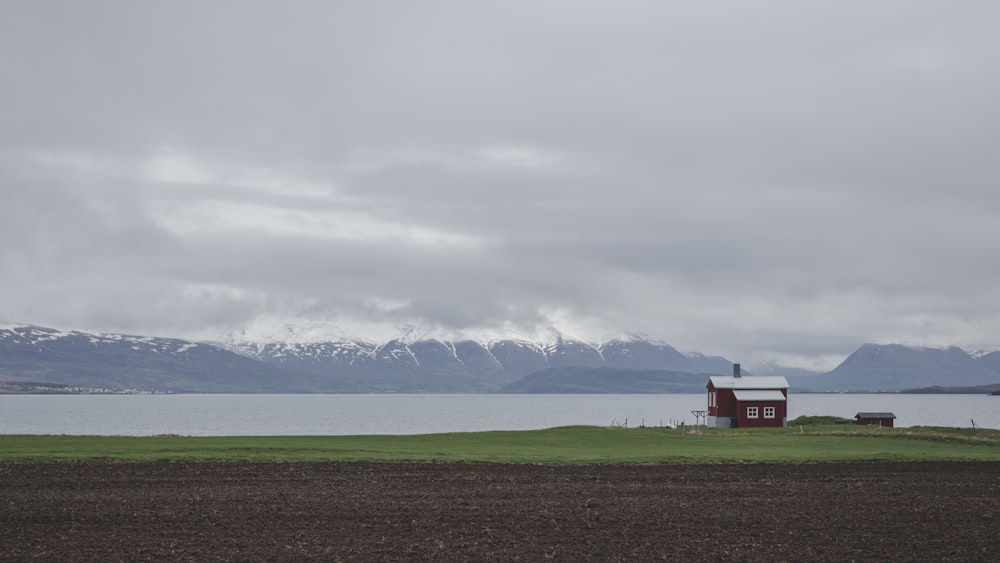 red house on green grass field near body of water under white clouds during daytime