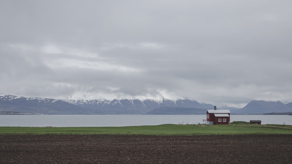 Casa roja en campo de hierba verde cerca del cuerpo de agua bajo nubes blancas durante el día