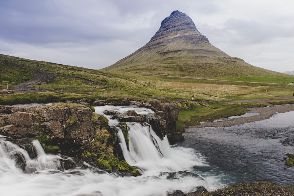 cascades près du champ d’herbe verte et de la montagne sous les nuages blancs pendant la journée