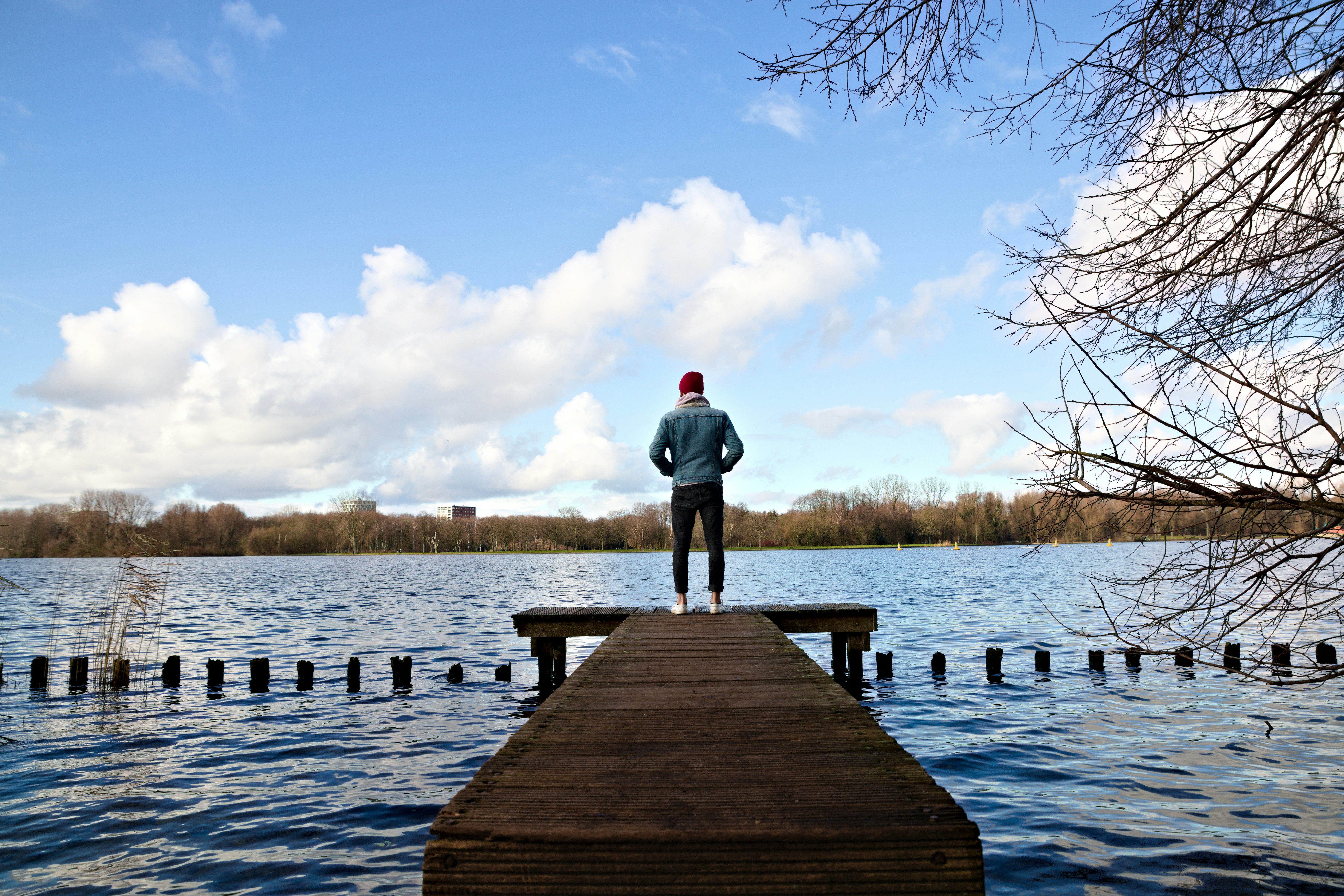 man in gray hoodie standing on wooden dock during daytime