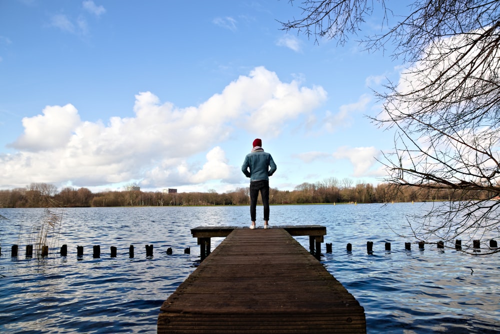 man in gray hoodie standing on wooden dock during daytime