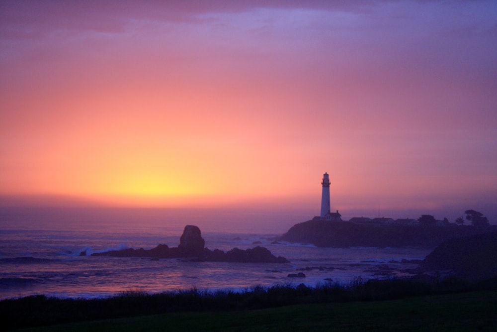 silhouette of lighthouse on seashore during sunset