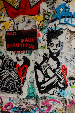 A vibrant collage featuring a mixture of graffiti, poster art, and street art. A prominent artwork of a person wearing boxing gloves labeled with 'Everlast' is central. The phrase 'BAD MADE BEAUTIFUL' appears in bold red and pink letters on a black background. Scattered graffiti and various symbols, including a red heart and a large red crown, cover the walls, all set against a multicolored, textured backdrop.
