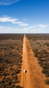 brown dirt road between green grass field under blue sky during daytime