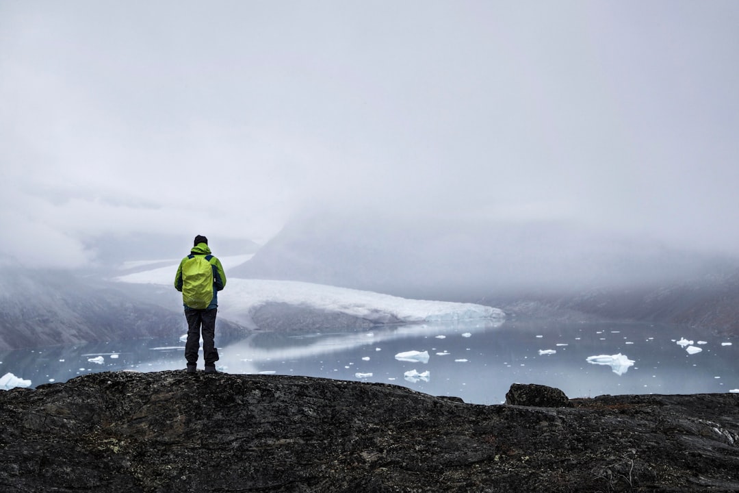 man in green jacket standing on rock formation near body of water