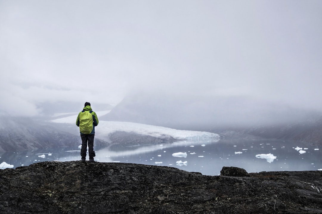 man in green jacket standing on rock formation near body of water,