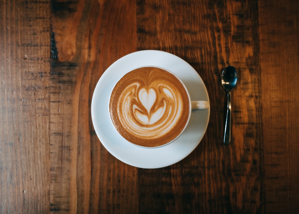 weiße Keramiktasse mit Untertasse auf braunem Holztisch